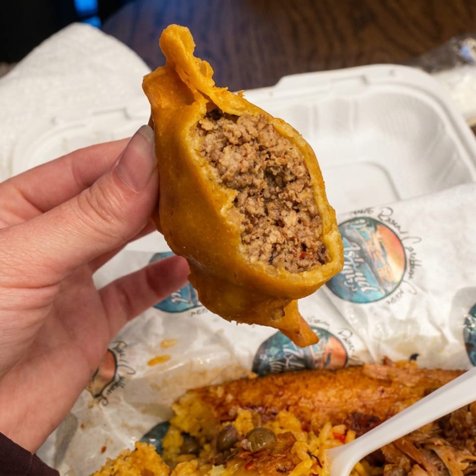 Hand holds a golden fried pastry cut open to reveal a savory minced meat filling over a takeout container.